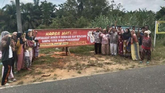 Masyarakat berdiri di depan spanduk bertuliskan "Harga Mati ,,,,!!!! Masyarakat Dusun IV Normark Siap berjuang Sampai Titik Darah Penghabisan"